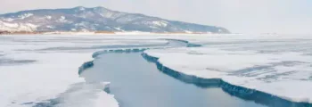 Glace craquelée sur un lac gelé avec des montagnes enneigées sous un ciel nuageux au loin, rappelant les paysages pittoresques près d'Irkutsk. - AEROAFFAIRES